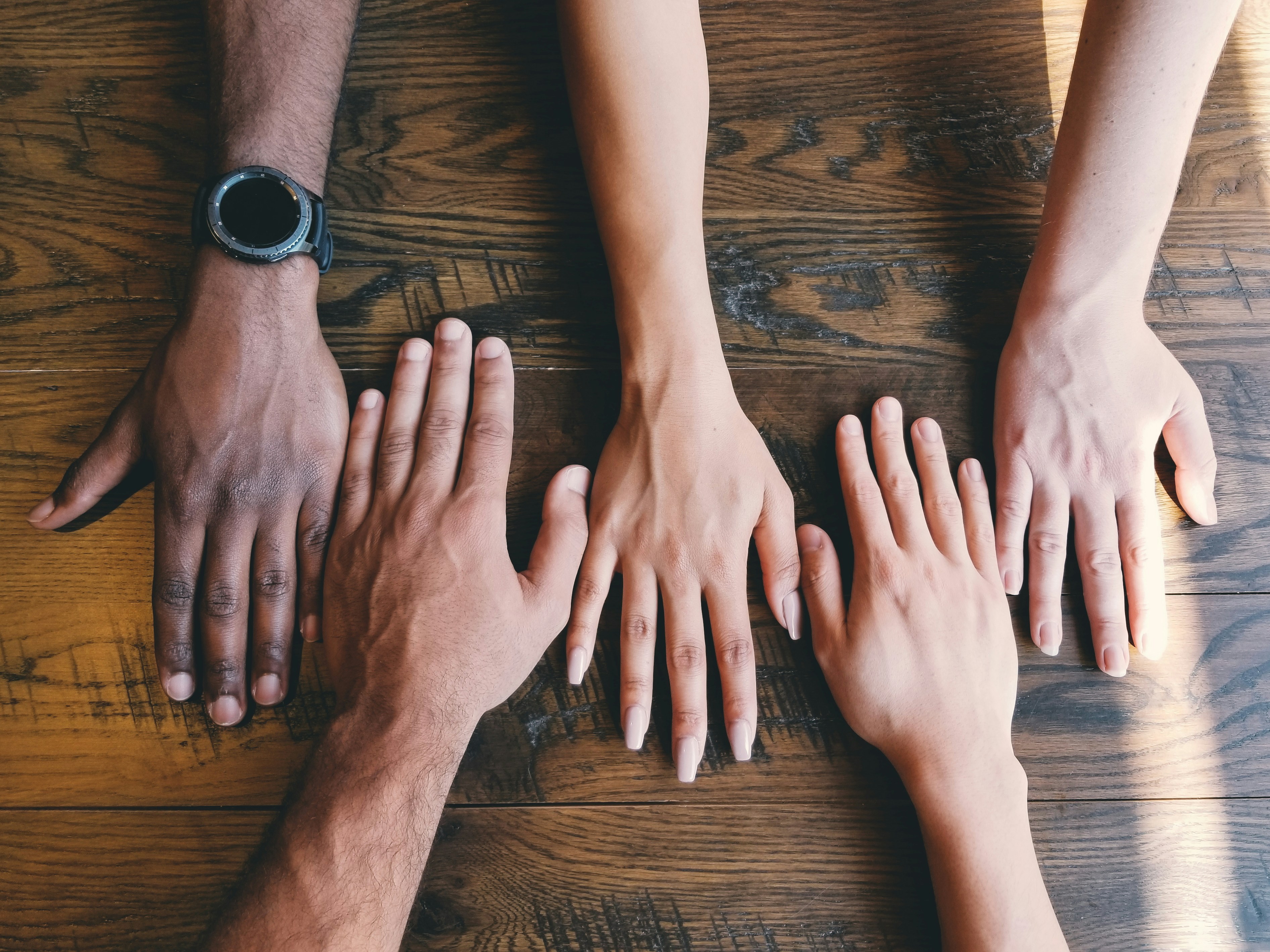 Top-down view of five diverse human hands placed side by side on a wooden table, symbolizing unity and teamwork