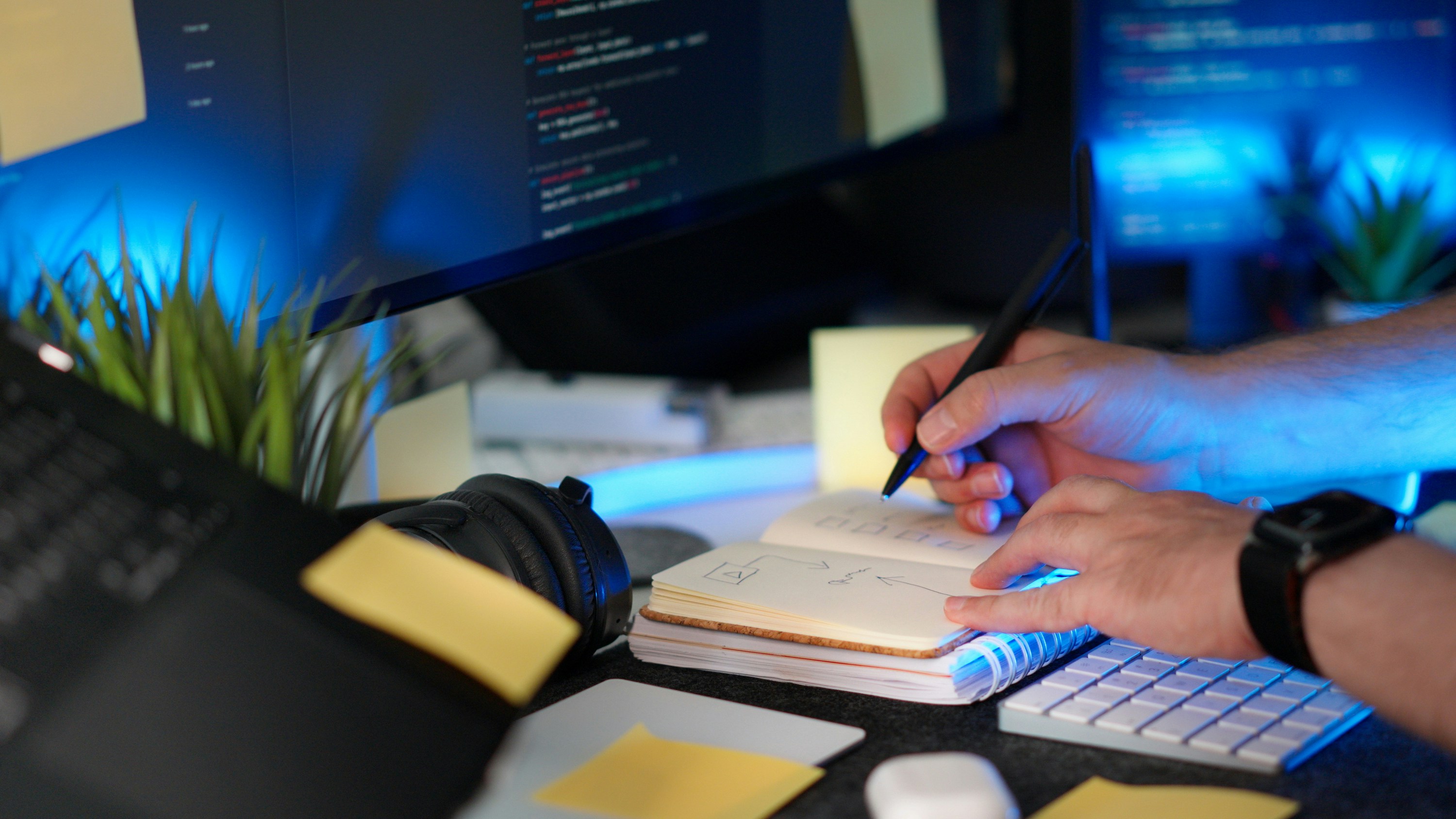 Close-up of a person coding on a screen while sketching ideas and notes into a notebook