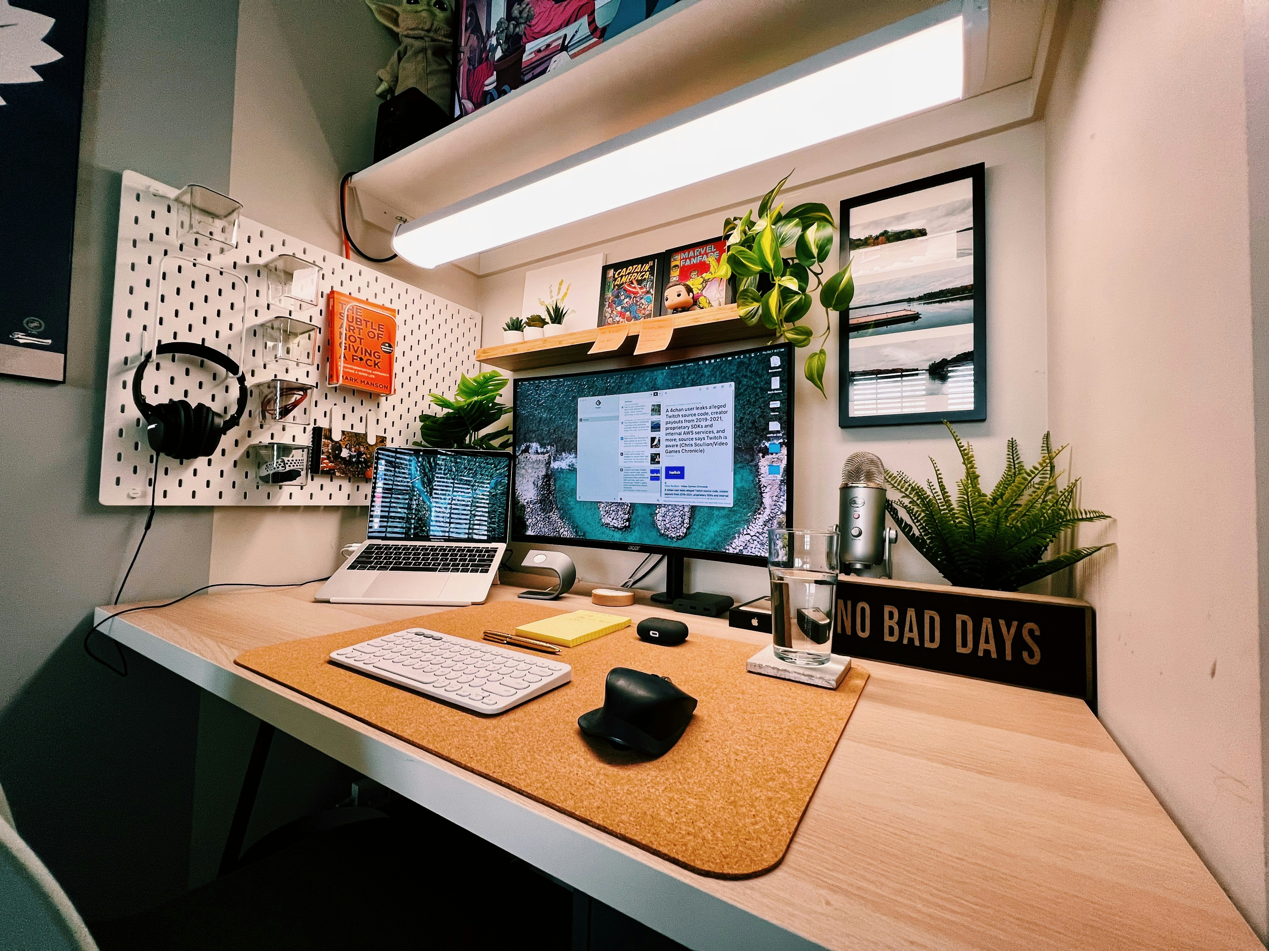 Modern workspace with a laptop, large monitor, desk mat, keyboard, and green plants